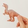 A hand holding a brown plastic dinosaur toy against a plain white background. Perfect for educational and creative uses.