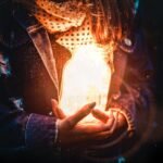 Artistic portrait of a woman holding a glowing jar, creating a magical light effect against a dark background.