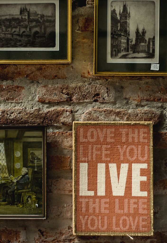 Art and frames adorn a rustic brick wall, featuring an inspirational quote on the canvas.